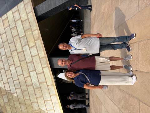 Three adults pose happily in front of a modern pyramid-shaped museum entrance in Cairo.
