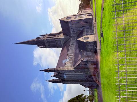 Stone Gothic-style cathedral with a tall spire rising above a manicured green lawn on a clear morning.