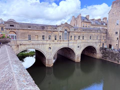 Historic stone bridge lined with Georgian buildings spanning a calm river in a classic English city.