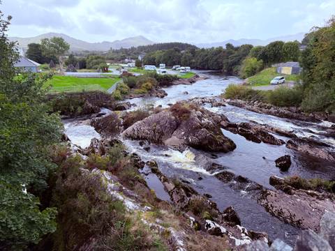 Rocky river rapids winding through lush countryside with scattered campers and rolling hills in the distance.