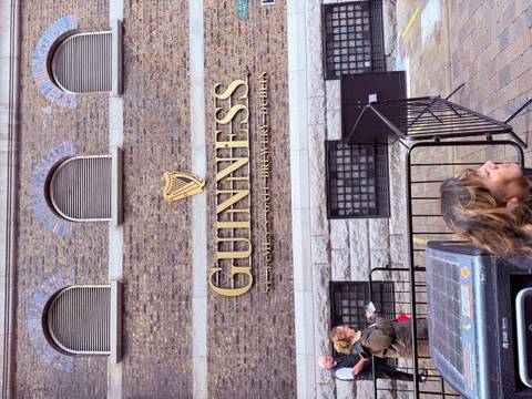 Exterior wall of the Guinness Storehouse with its iconic gold harp logo and visitors milling about.