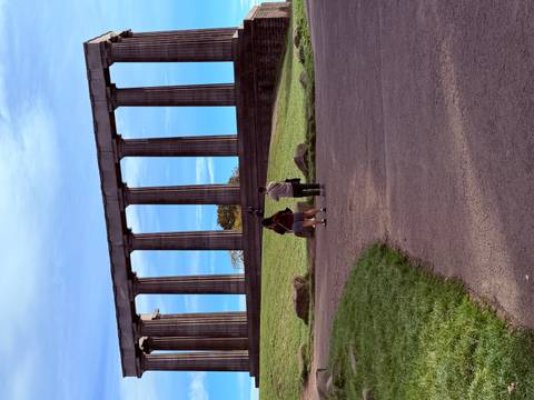 Two visitors walking toward neoclassical columns of the National Monument on a grassy hill under blue skies.