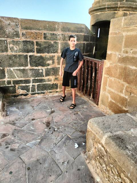Cropped image of a boy’s lower body standing in a weathered stone nook, offering minimal context.