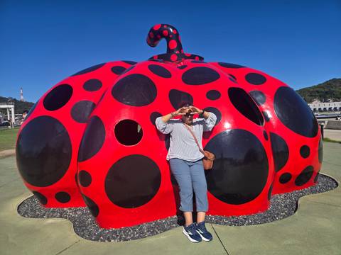 A woman forms a heart with her hands in front of Yayoi Kusama’s red-and-black polka-dot pumpkin sculpture.