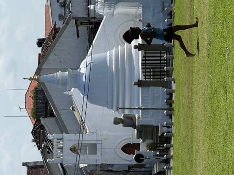 A runner passes a small white stupa and seated Buddha statue on a grassy field in a Sri Lankan town.