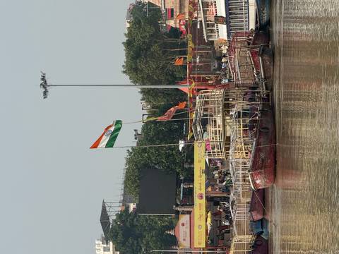 Wooden boats moor along the Ganges River ghats beneath a large Indian flag fluttering in Varanasi.