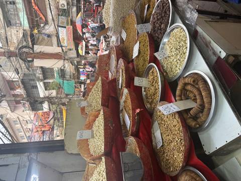 A bustling street-market stall displays mounds of nuts and dried fruit with handwritten price tags.