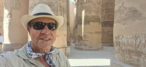 A man in a Panama hat takes a selfie among towering hieroglyph-covered columns at Karnak Temple.