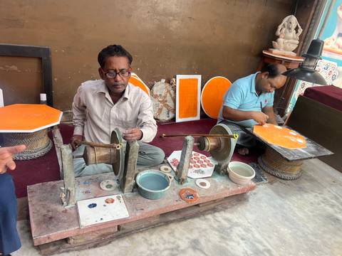 Local craftsmen seated indoors shaping and polishing decorative marble pieces using traditional tools.