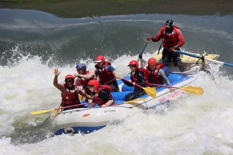Excited rafters in red helmets navigating white-water rapids in an inflatable raft.