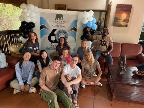 Tour group seated indoors posing in front of a 60th anniversary banner at a safari lodge.