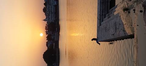Lone person sits on a pier overlooking a calm lake at a golden sunset.