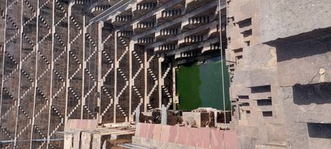 Geometric terraced steps of Chand Baori stepwell descend to green water.