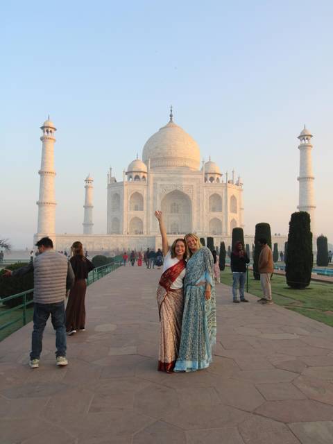 Two women in saris celebrating before Taj Mahal at early morning light