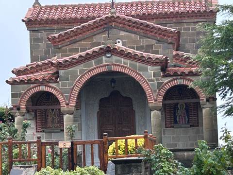 Small stone chapel with red-tiled arches and wooden door set against greenery.