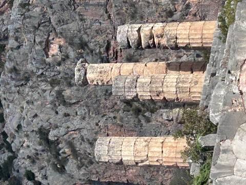 Weathered ancient stone columns standing before a rugged mountain cliff.