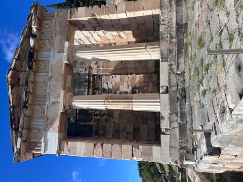 Front view of a small classical Greek temple ruin with Doric columns under blue sky.