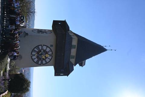 Historic Uhrturm clock tower on hilltop above Graz with large tour group gathered below.