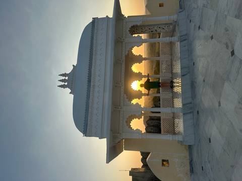Silhouette of a person framed by ornate arches catching the setting sun from a white marble pavilion.