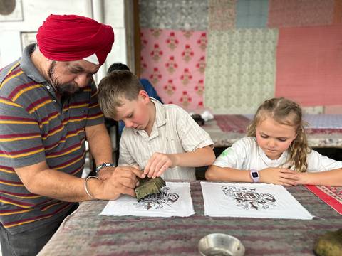 Sikh artisan helps two children create block prints on fabric inside a colorful workshop.
