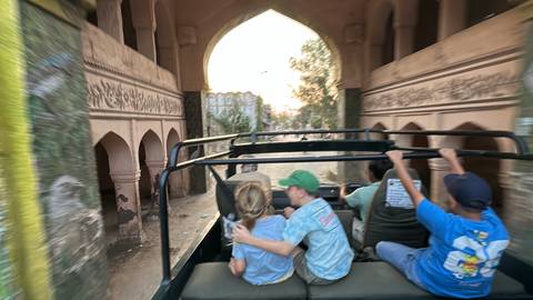 Motion-blurred view from the back of a jeep passing under an old arched gateway at dusk.