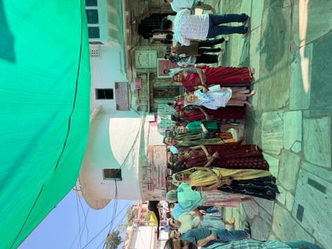 Tourist family and local women dressed in saris pose together under a green canopy in a temple courtyard.