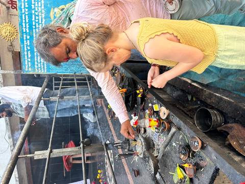 A girl and a man light incense offerings at a busy shrine filled with small oil lamps and smoke.