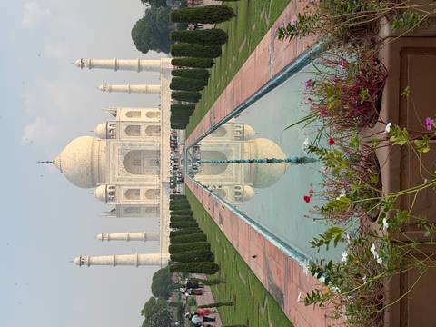 Centered view of the Taj Mahal perfectly reflected in the long pool framed by gardens and flowers.