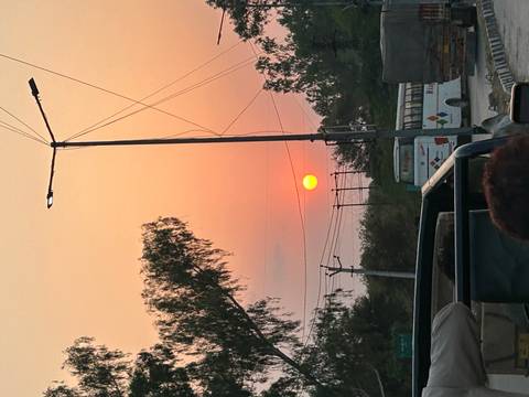 Orange sun setting behind roadside power lines and buses viewed from a moving vehicle.