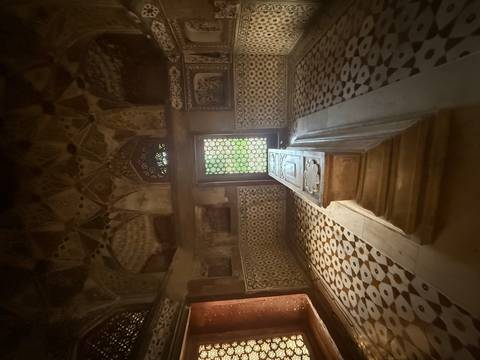 Dimly lit interior chamber with an ornate stone cenotaph and patterned marble floor inside the Taj Mahal complex.