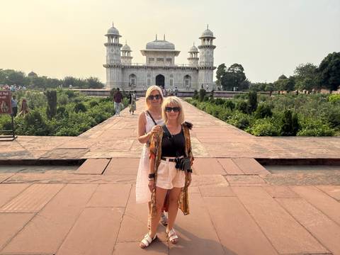 Two women posing on a red sandstone pathway with the white marble Itimad-ud-Daulah mausoleum behind them.
