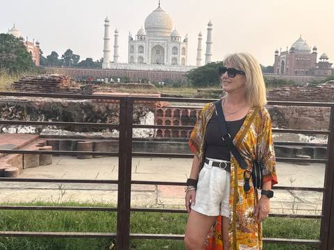 A woman standing near ruins with the Taj Mahal visible across the lawn in the background.