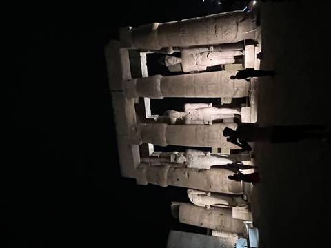 Nighttime view of towering illuminated statues in Luxor Temple with visitors silhouetted below.