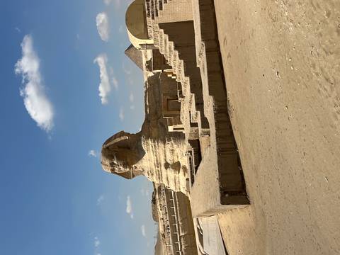 Iconic Sphinx statue with a pyramid in the background under a bright blue sky.