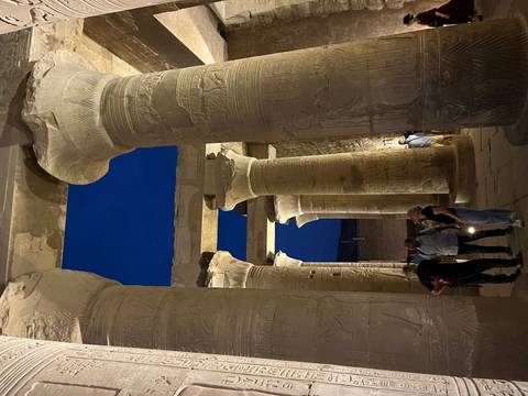 Evening view through the massive columned hall of Kom Ombo Temple with visitors exploring.