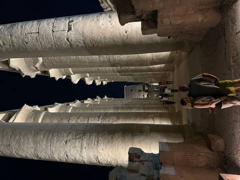 Tall illuminated colonnade in Luxor Temple with a couple posing in the foreground at night.