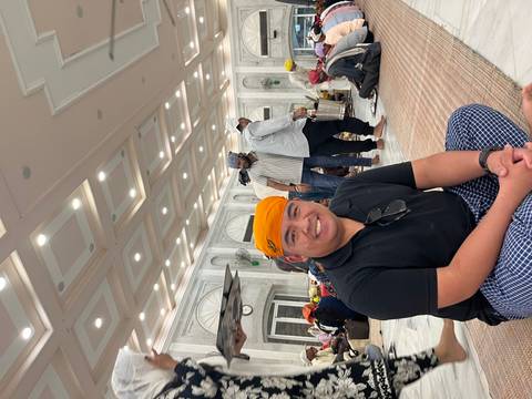 Visitors sit cross-legged inside a bright marble hall of a Sikh Gurdwara wearing headscarves.