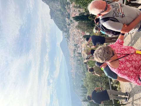 Tour group taking photos over Taormina rooftops toward hazy Mount Etna.