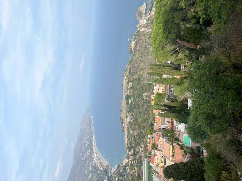High coastal panorama over Taormina and the turquoise Ionian Sea with cypress trees in foreground.