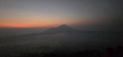 Pre-dawn silhouette of a volcanic peak against a faint orange horizon.