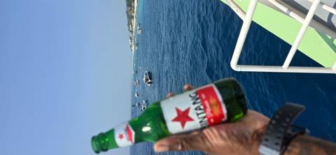 A hand holds a Bintang beer bottle against a backdrop of blue sea dotted with boats.