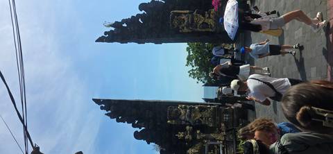 Crowds gather at the split stone gate of Tanah Lot temple complex under bright skies.