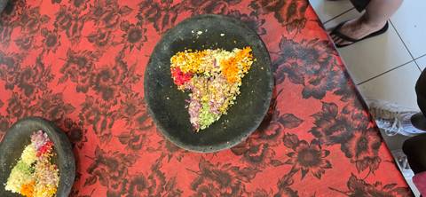 Crushed flower petals arranged in a heart shape on a black stone plate atop a red patterned tablecloth.