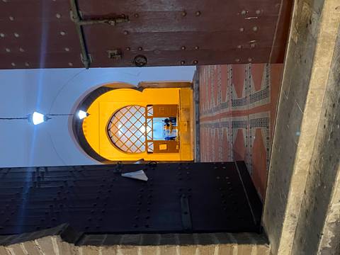 Dimly lit arched doorway reveals a brightly illuminated hall with patterned tiles and hanging lanterns.
