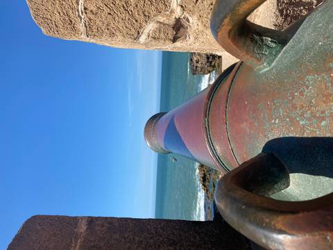 Weathered bronze cannon points toward the Atlantic from ancient ramparts under a vivid blue sky.