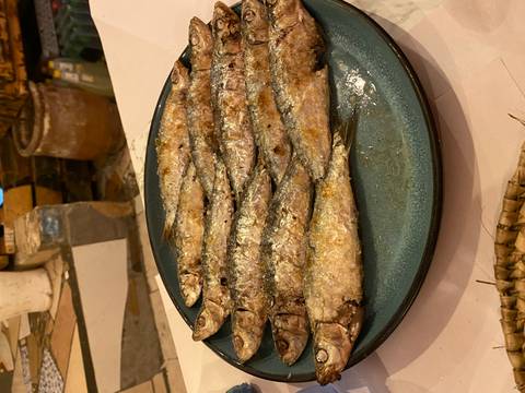 Plate of grilled whole sardines served on a rustic ceramic dish in warm indoor lighting.