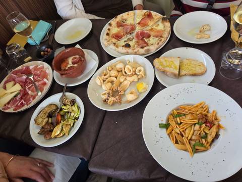 Table laden with Italian antipasti, pasta, pizza and fried seafood ready for a shared meal.