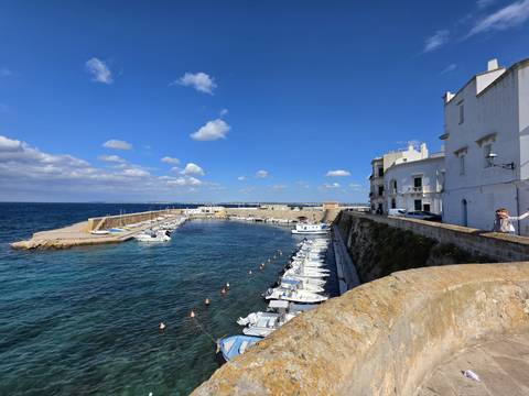 Bright blue harbour with small fishing boats moored along ancient sea walls on a clear day.