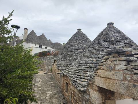 Close-up of the grey stone cone roofs of several trulli against an overcast sky.