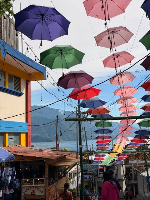 Strings of vivid umbrellas hang above power lines with mountain scenery in the background.